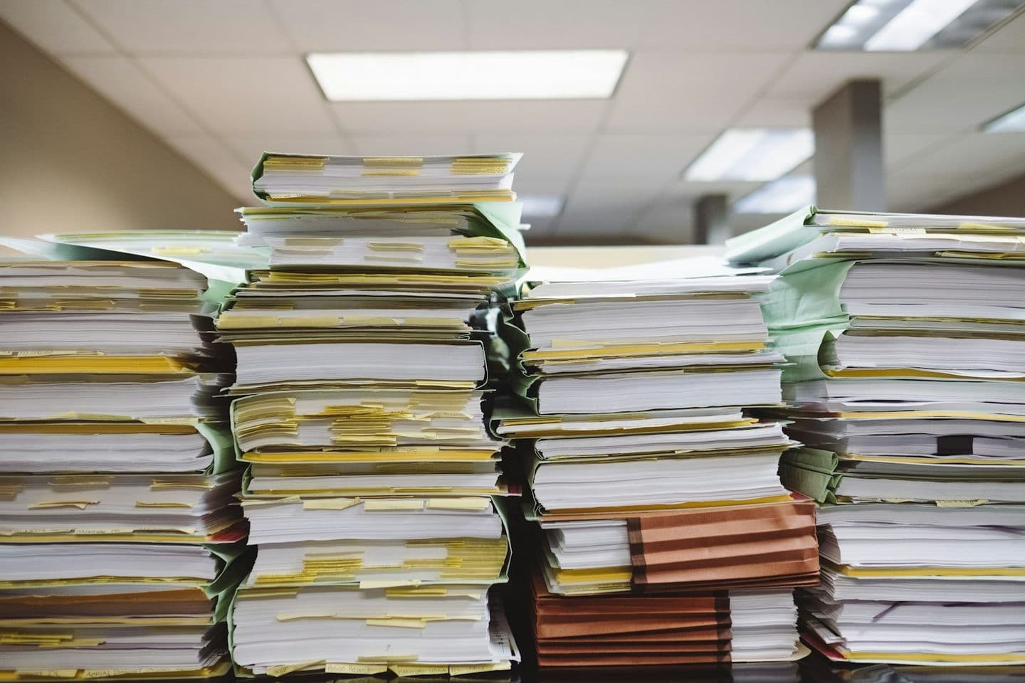 Pilas de expedientes y carpetas de papel acumuladas sobre una mesa de oficina.