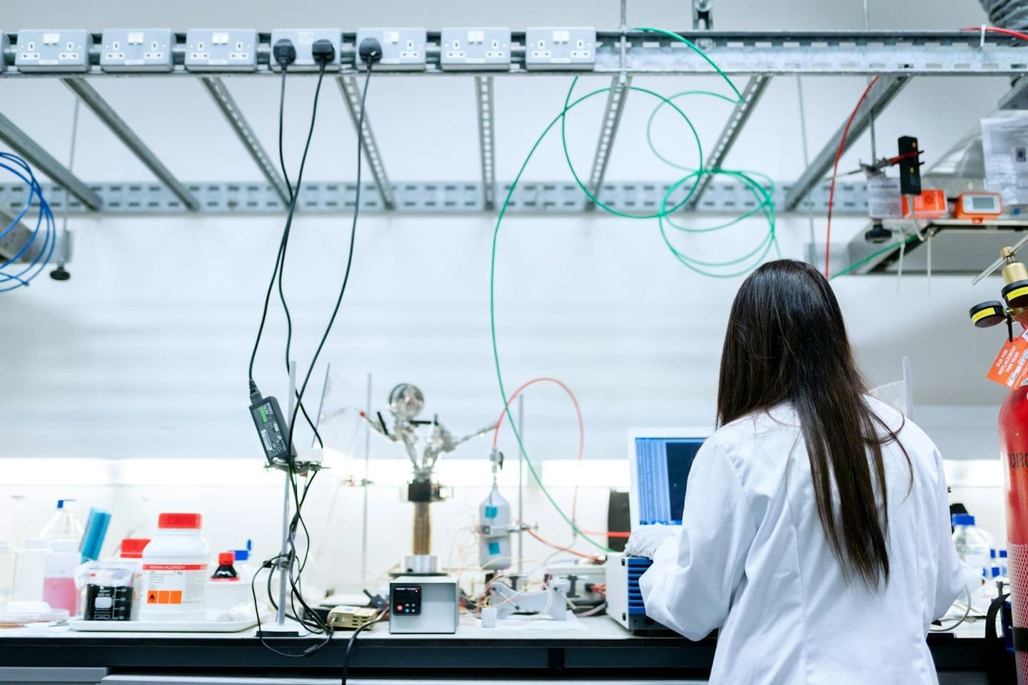 Una investigadora con bata blanca trabaja con un portátil en un laboratorio de ingeniería química.